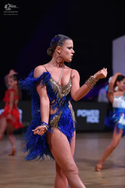 Dancesport competitor: Female dancer in foreground: blue and gold Latin dress with blue feather fringe 