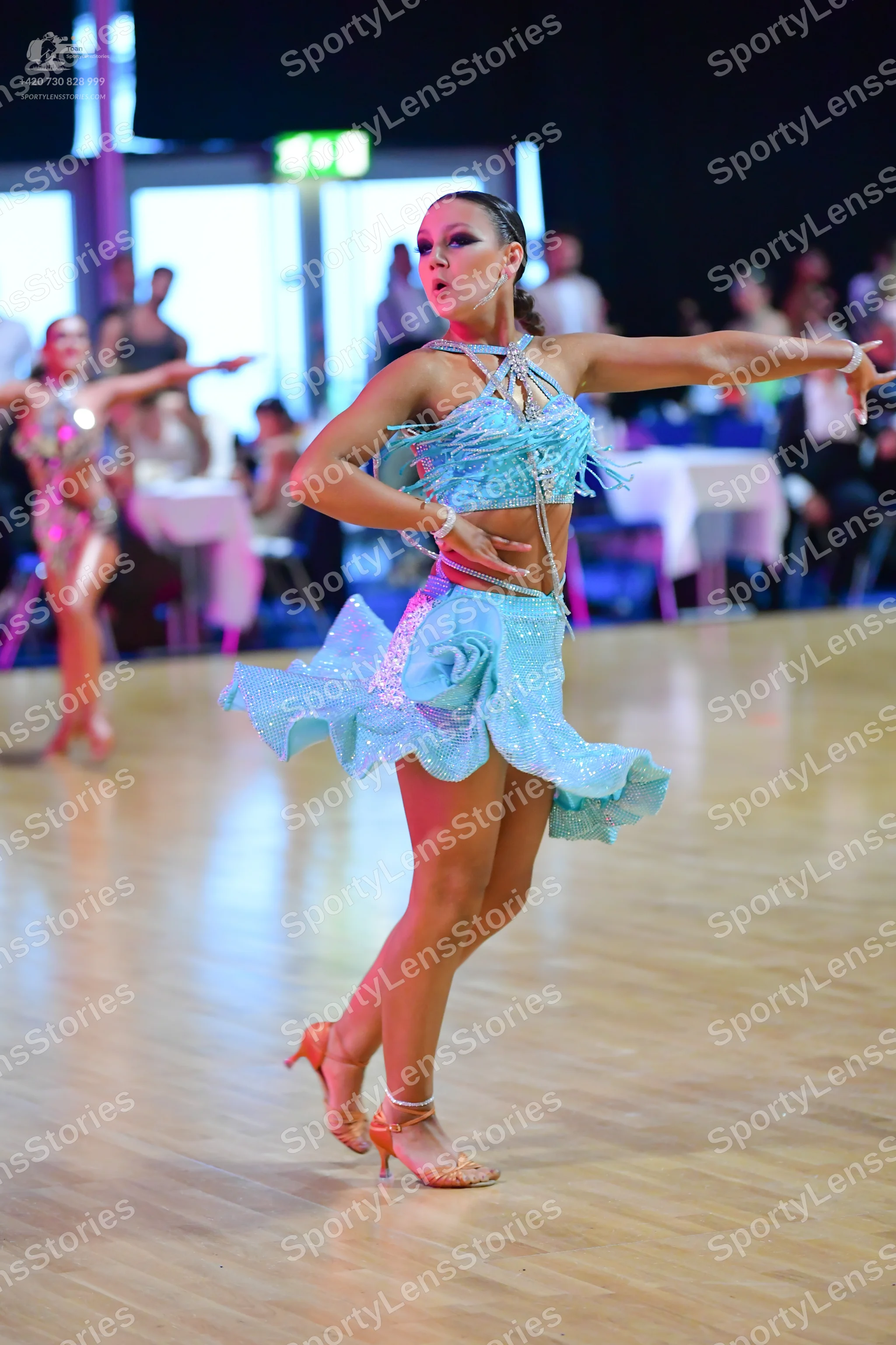 Dancesport competitor: Female dancer in foreground: light blue sequined Latin dance costume consisting
