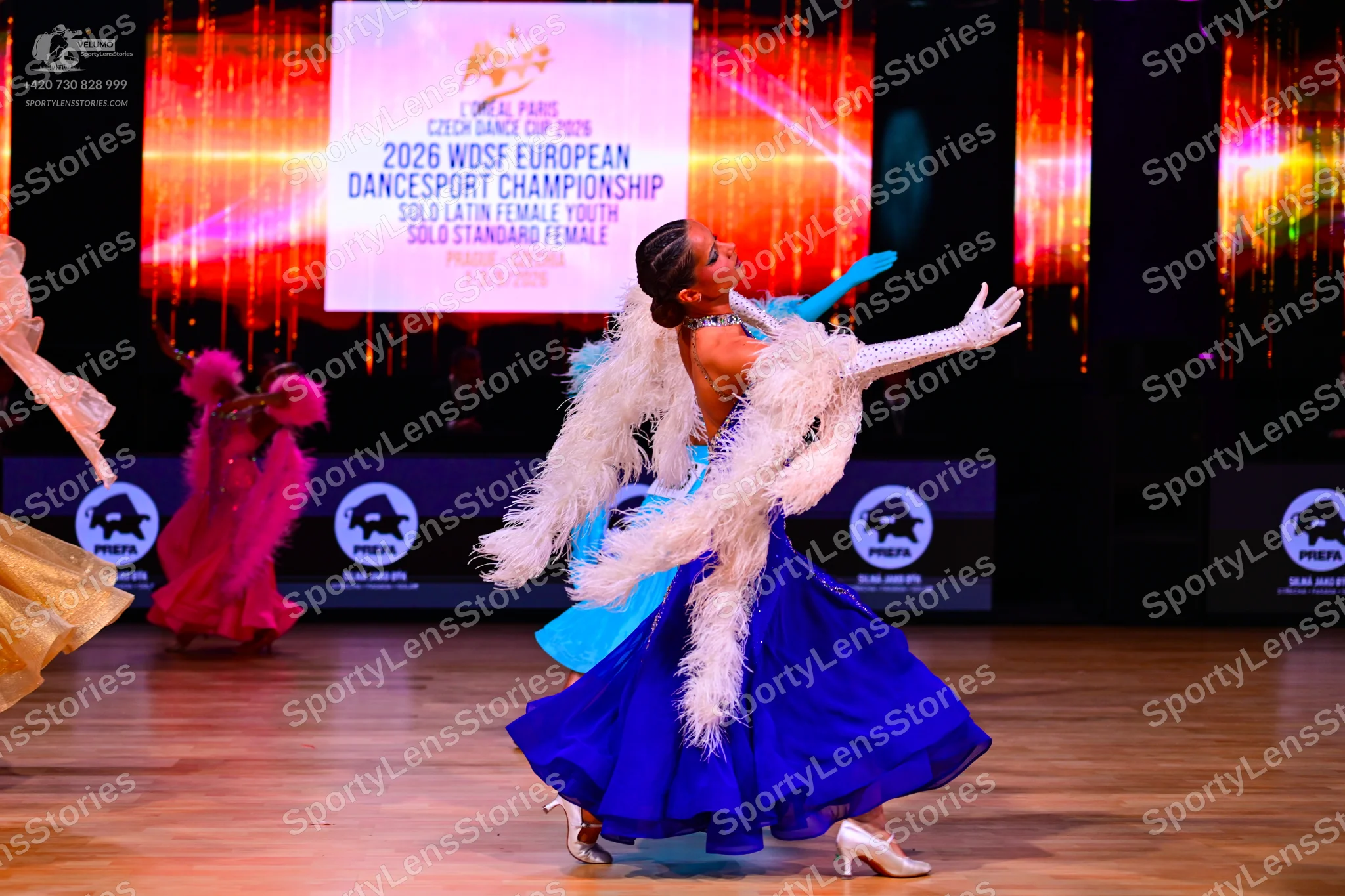 Dancesport competitor: Female dancer: royal blue ballgown with a voluminous skirt, featuring a white fe