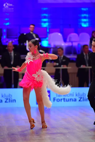 Dancesport competitor: Female dancer: bright pink latin dress with white floral/feather decorations and