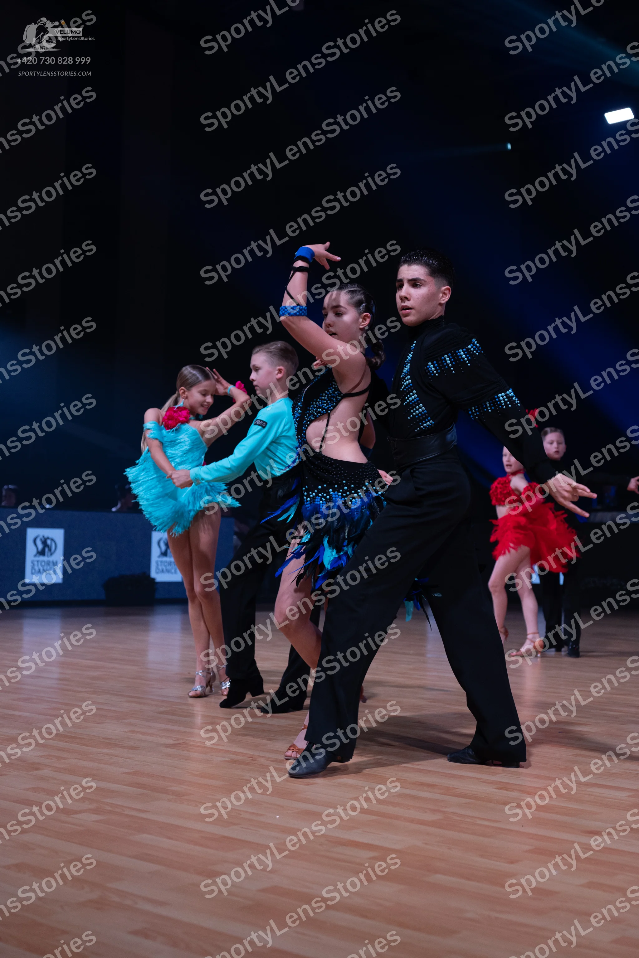 Dancesport competitor: Female dancer (far left): light blue/cyan latin dress with a ruffled skirt
