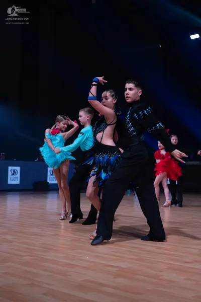 Dancesport competitor: Female dancer (far left): light blue/cyan latin dress with a ruffled skirt