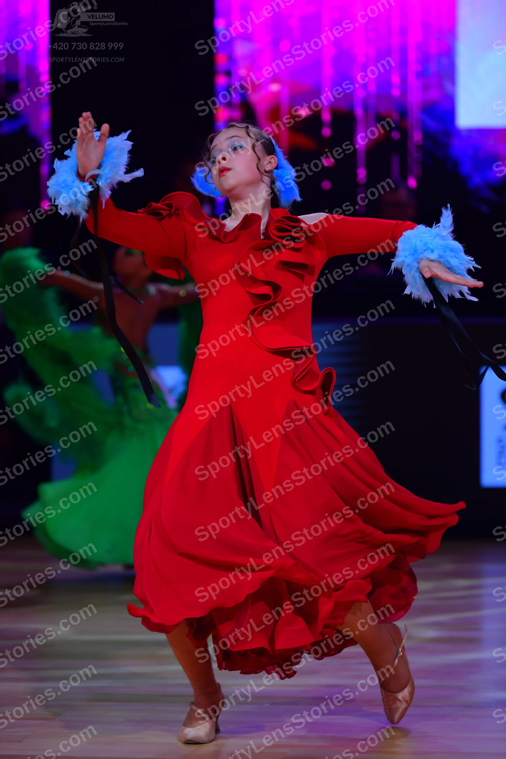 Dancesport competitor: Female dancer in foreground: red long-sleeved Latin dance dress with large diago