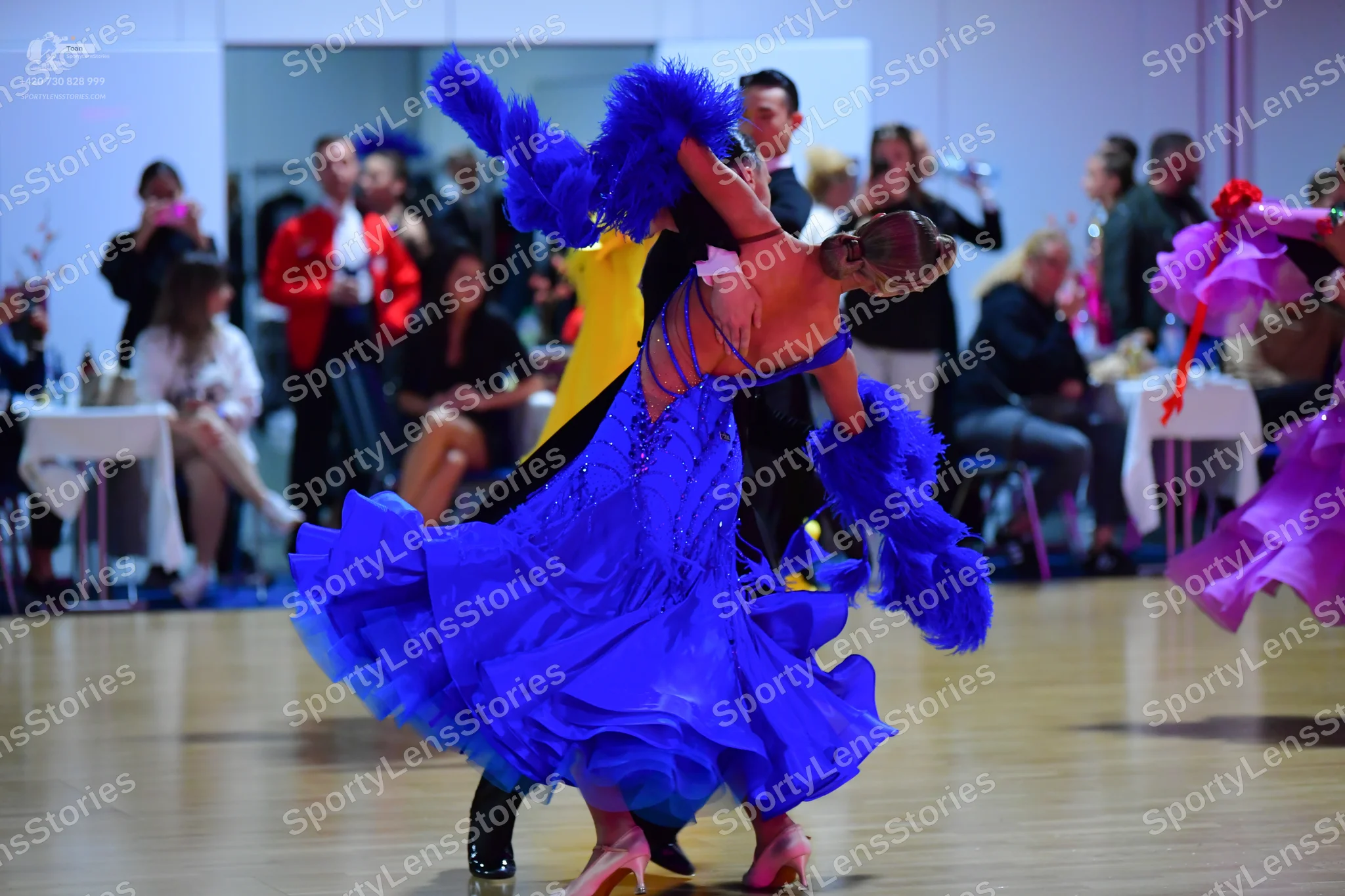 Dancesport competitor: Female dancer: vibrant blue Latin dance dress with voluminous, flowing layers an