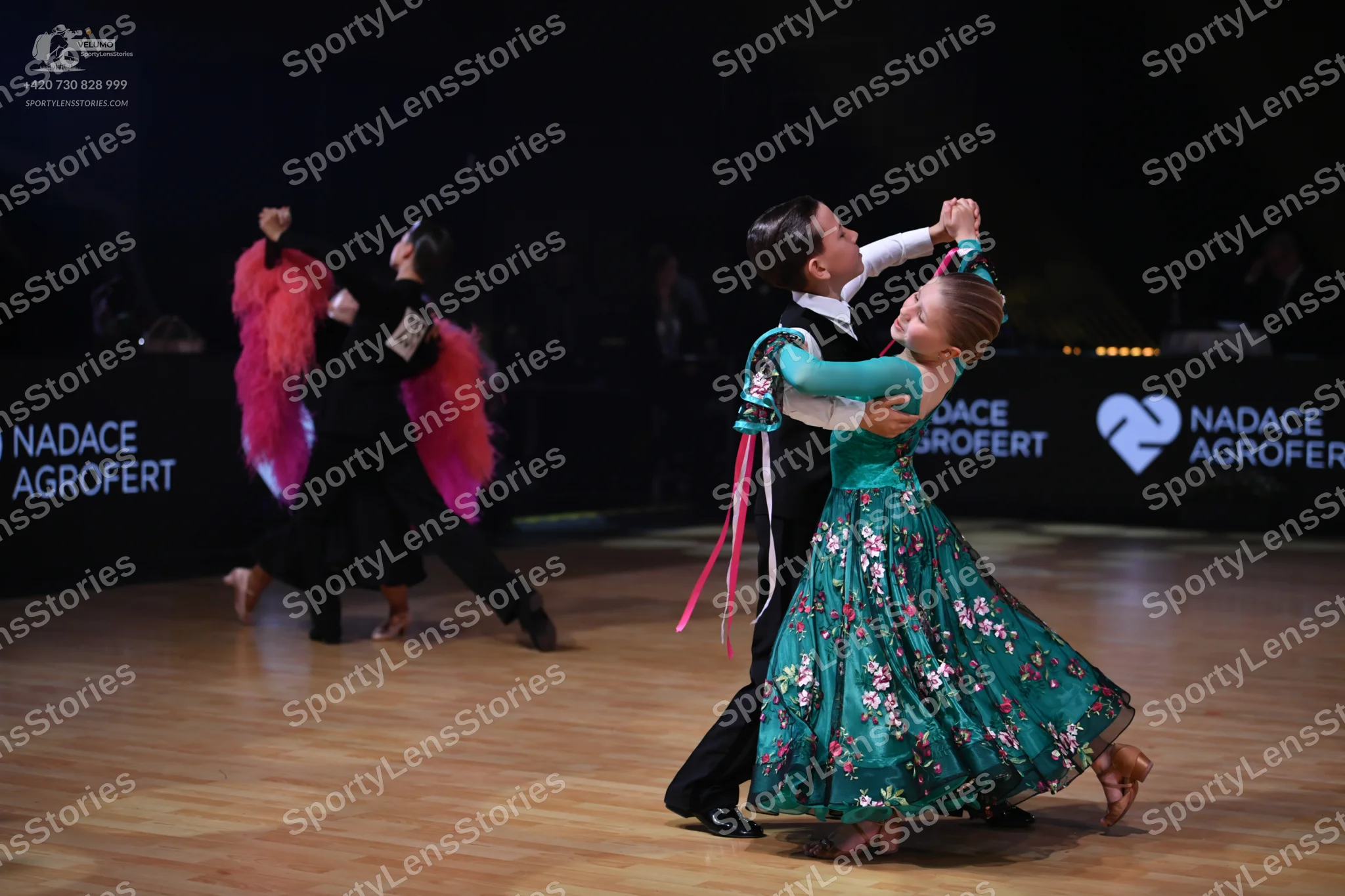 Dancesport competitor: Left female dancer: black Latin dance dress with voluminous pink feather or frin