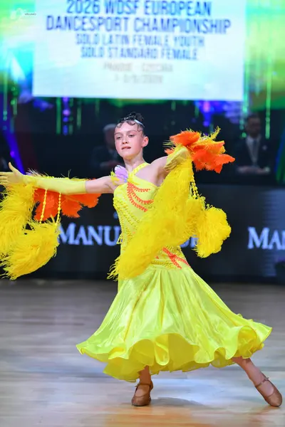 Dancesport competitor: Female dancer: yellow Latin dress with orange/red trim and large yellow feathere
