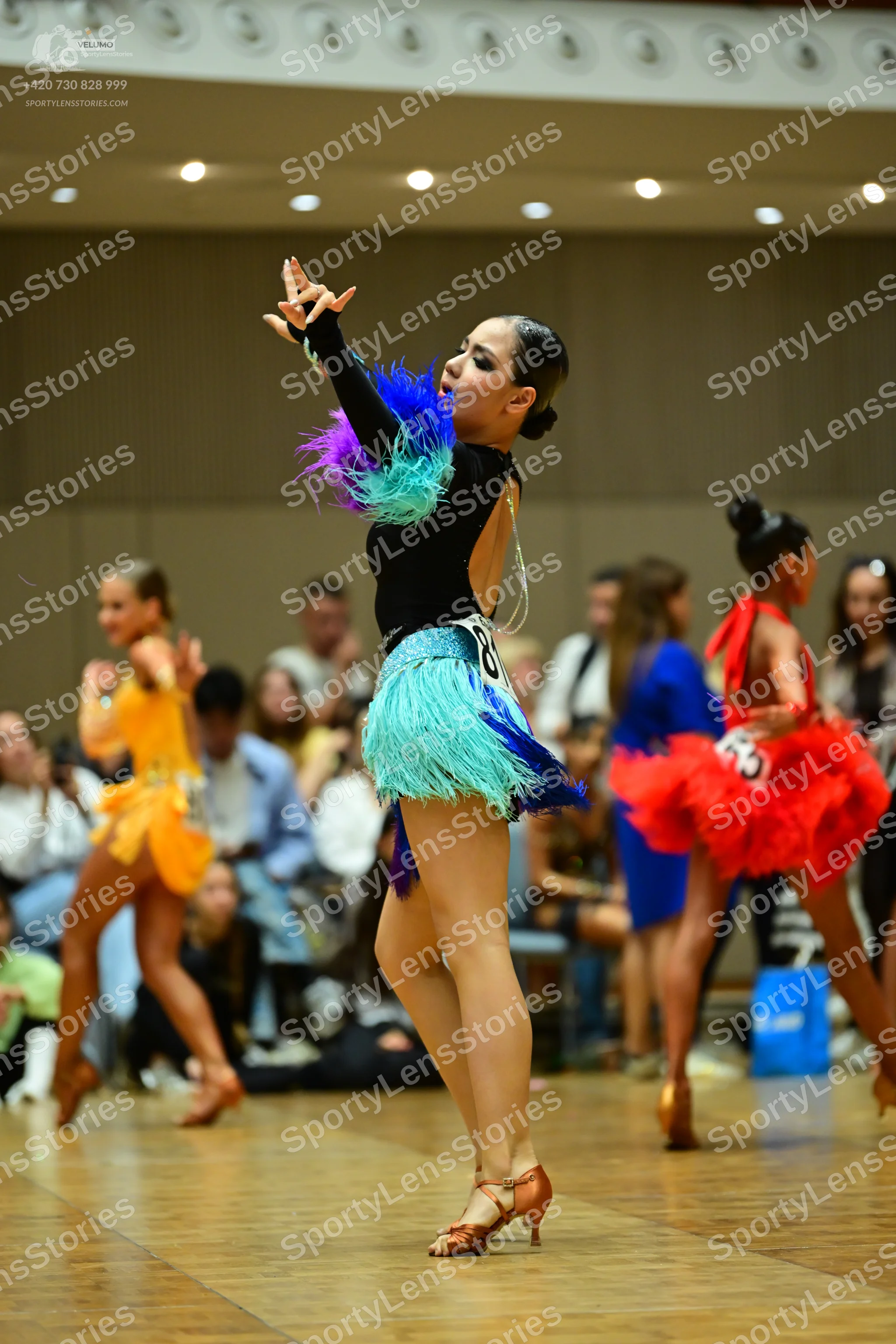 Dancesport competitor: Female dancer in center: black long-sleeved Latin costume with colorful feathers