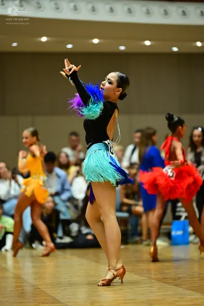 Dancesport competitor: Female dancer in center: black long-sleeved Latin costume with colorful feathers
