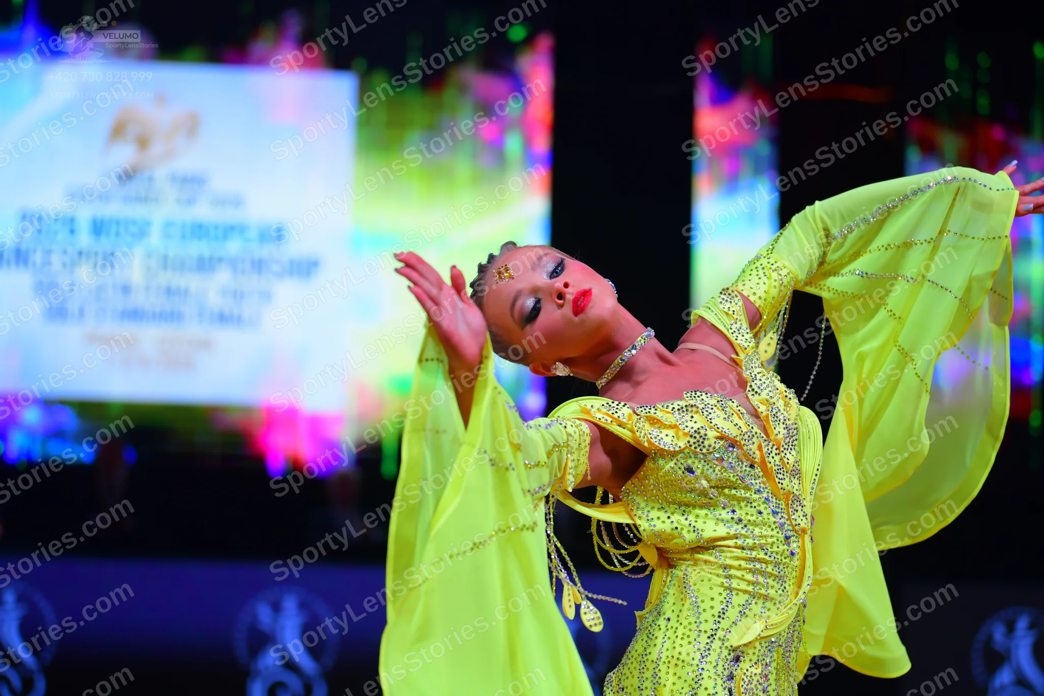 Dancesport competitor: Female dancer: bright yellow/lime green Latin dance dress with long, wide, flowi