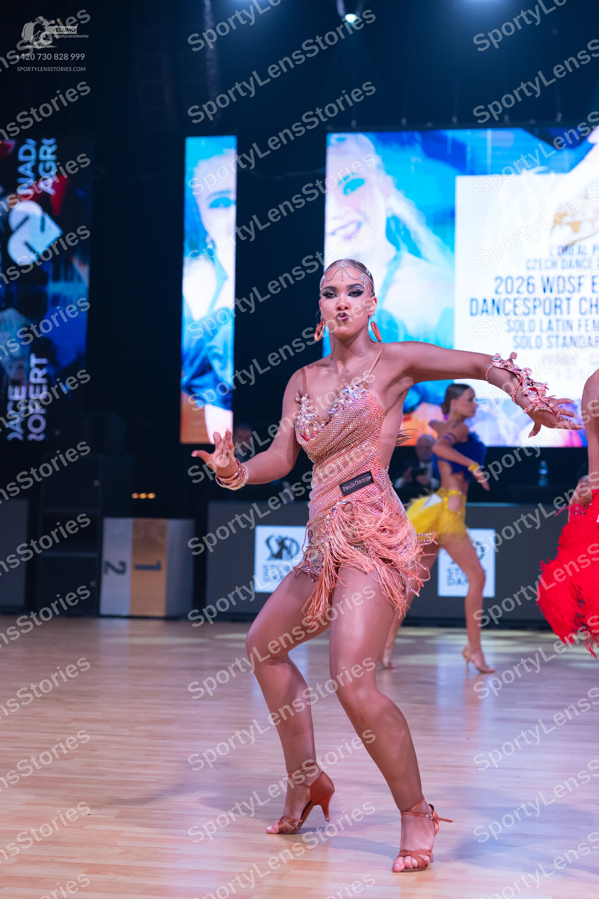 Dancesport competitor: Female dancer in foreground: champagne-colored Latin dress with sequins, beads,