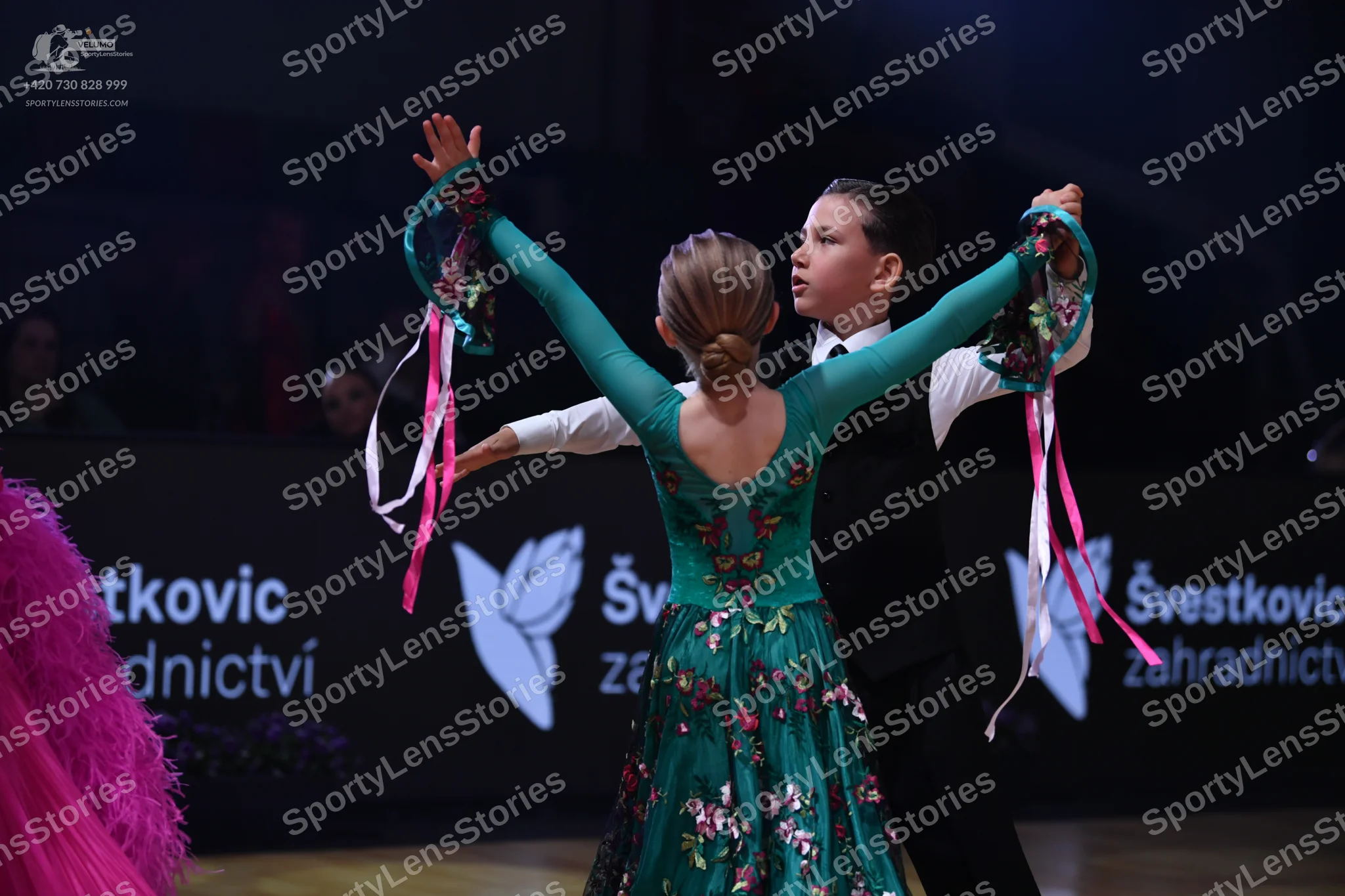Dancesport competitor: Female dancer: teal long-sleeved dress with a floral pattern and long pink and w