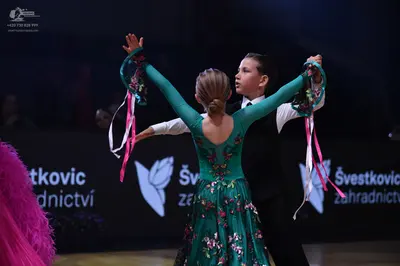 Dancesport competitor: Female dancer: teal long-sleeved dress with a floral pattern and long pink and w