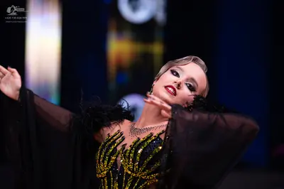 Dancesport competitor: Female dancer: black and gold sequined Latin dance bodice with sheer dark sleeve