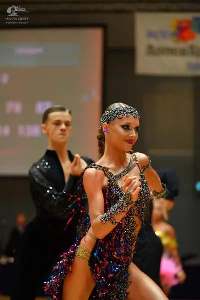 Dancesport competitor: Female dancer: dark blue, purple, and gold sequined Latin dress with a matching 