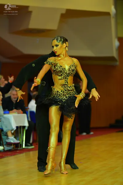 Dancesport competitor: Female dancer: leopard print Latin dress with black feather trim, gold strappy h