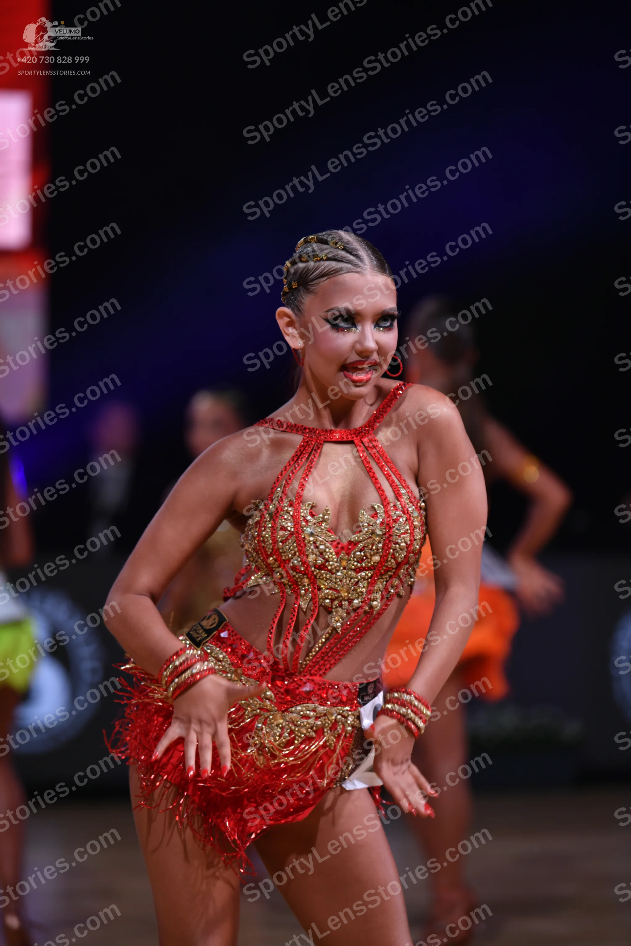 Dancesport competitor: Female dancer (foreground): red Latin dress with gold and silver sequin/bead emb