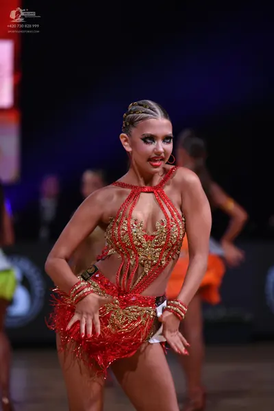 Dancesport competitor: Female dancer (foreground): red Latin dress with gold and silver sequin/bead emb