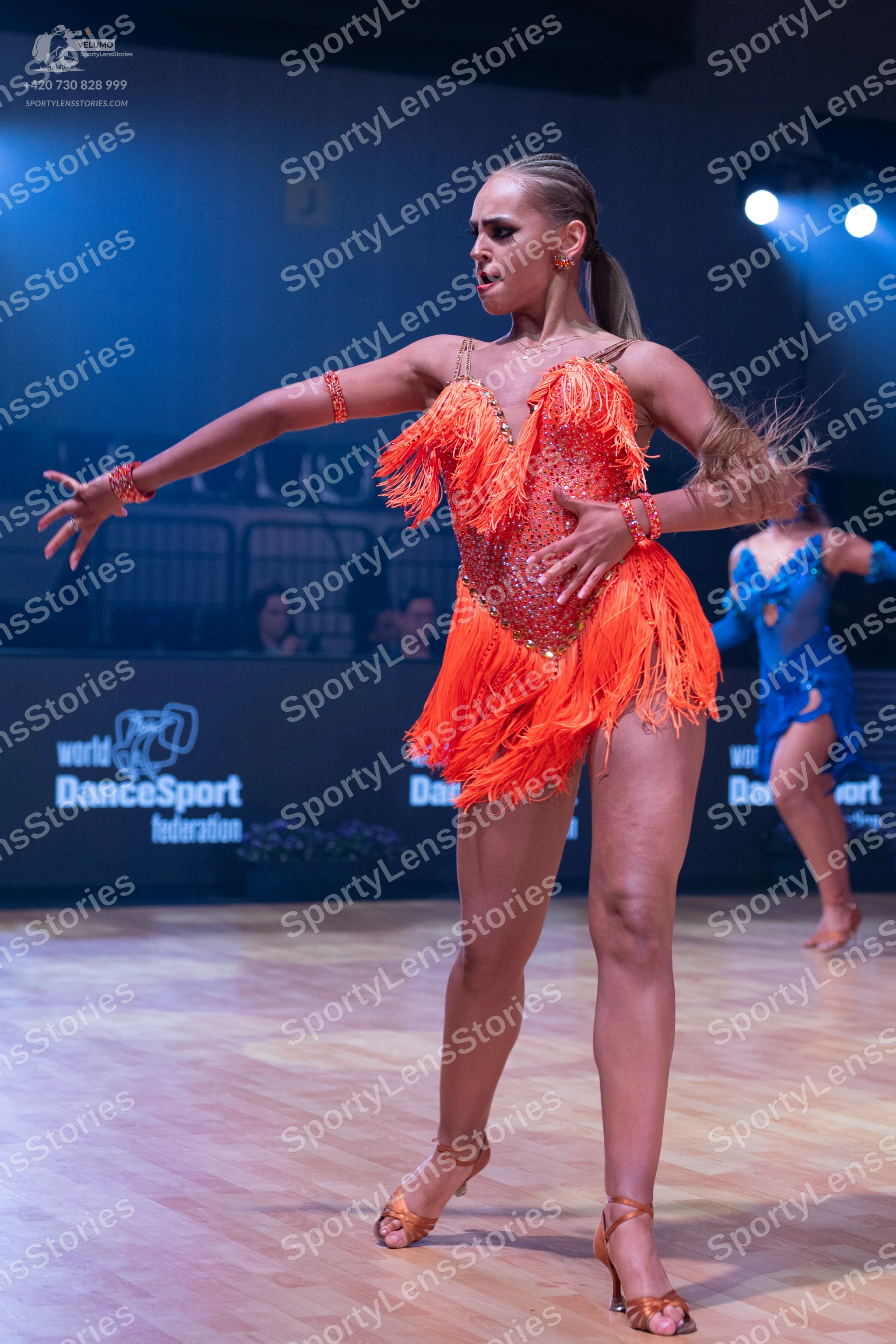 Dancesport competitor: Female dancer in foreground: orange latin dress with fringe and sequins, matchin