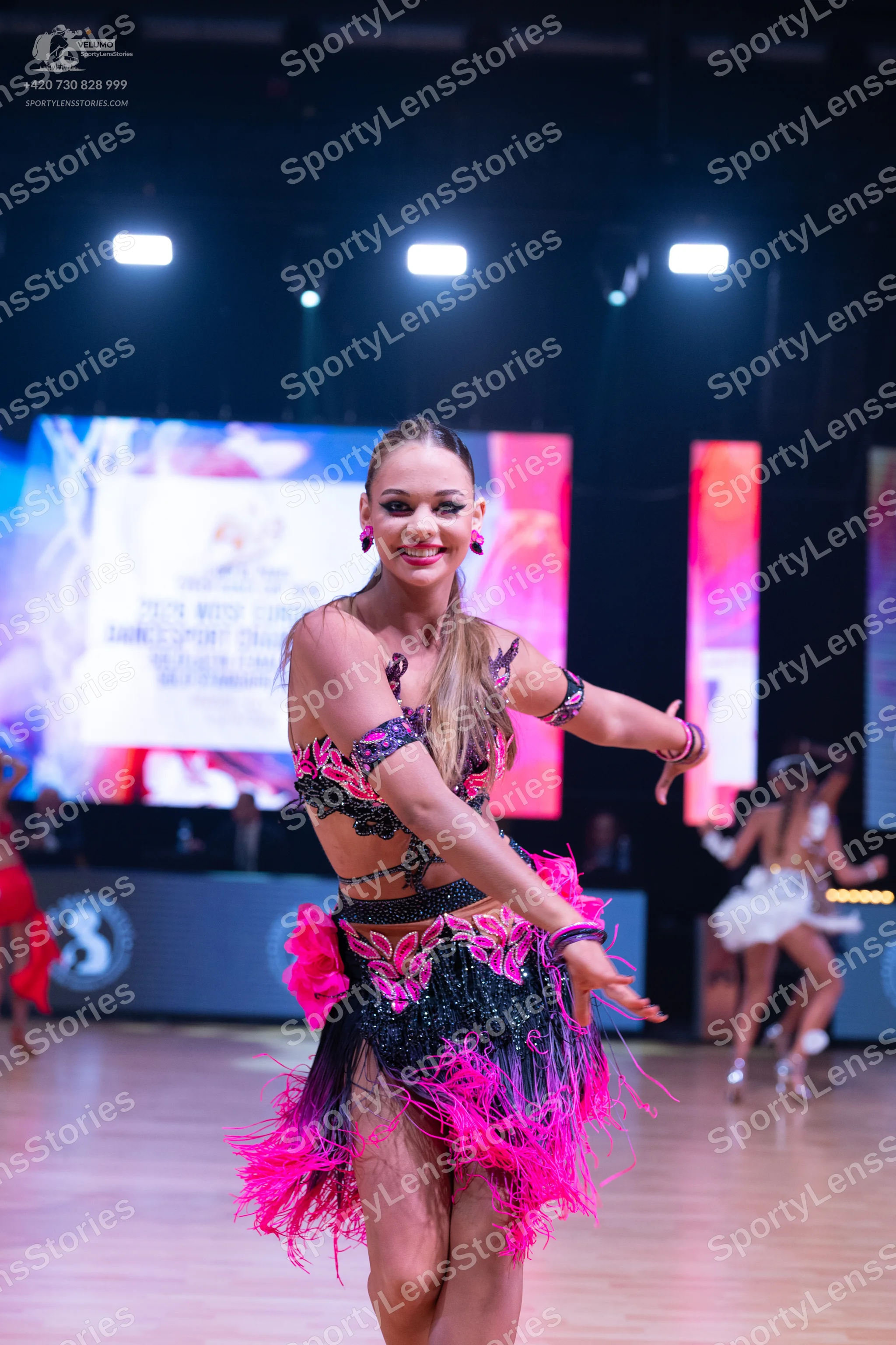 Dancesport competitor: Female dancer in foreground: black and bright pink two-piece latin costume with