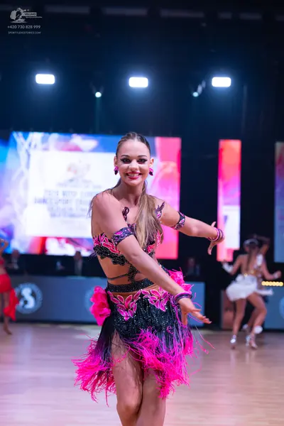 Dancesport competitor: Female dancer in foreground: black and bright pink two-piece latin costume with 