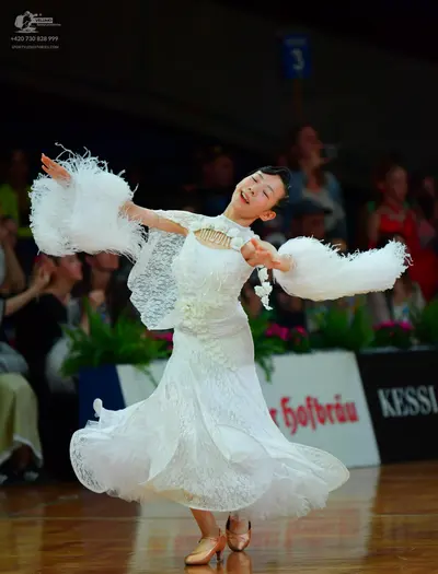 Dancesport competitor: Female dancer: white lace ballgown with large, white, fluffy, feather-like sleev