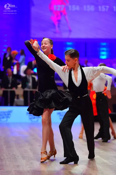 Dancesport competitor: Female dancer: black latin dress with a ruffled skirt and a red flower accessory