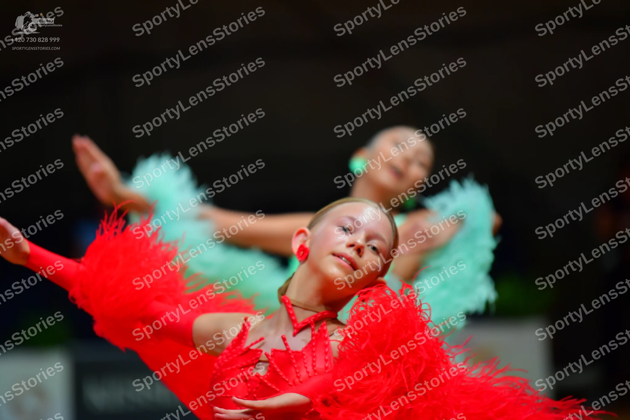 Dancesport competitor: Female dancer in foreground: red latin dress with long red feather-like fringe a