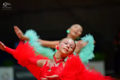 Dancesport competitor: Female dancer in foreground: red latin dress with long red feather-like fringe a