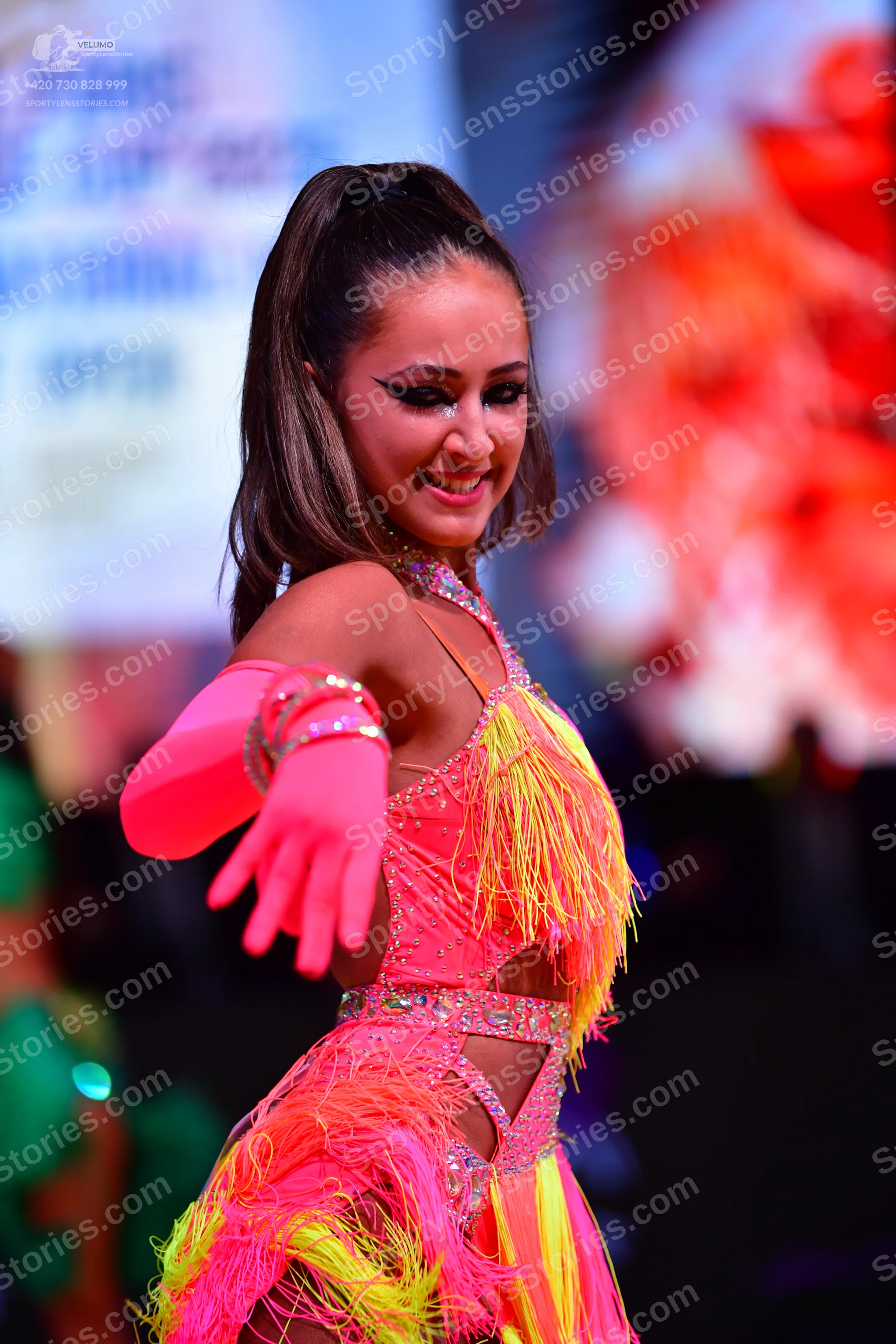 Dancesport competitor: Female dancer: neon pink and yellow Latin dress with fringe and rhinestone embel