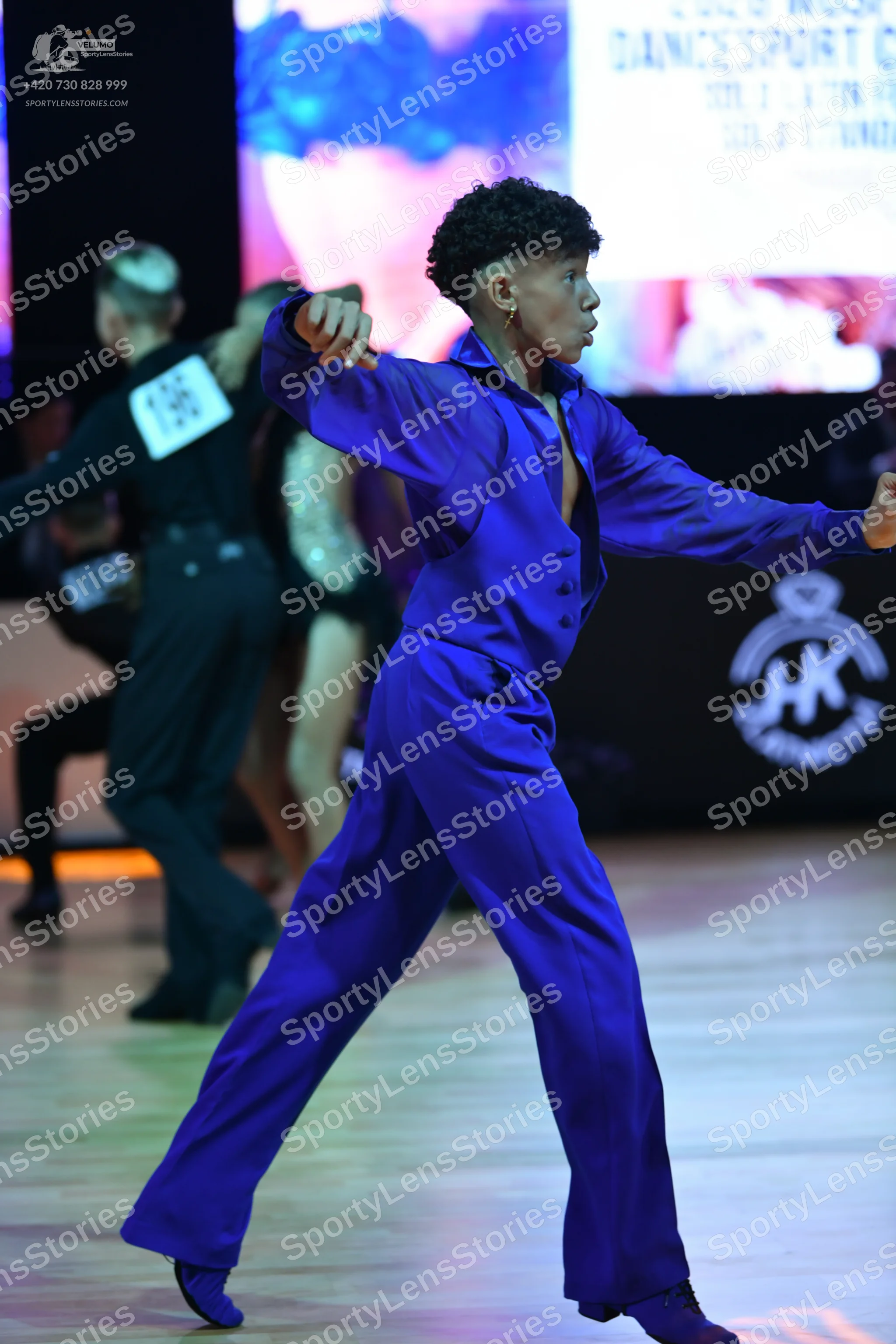 Dancesport competitor: Male dancer (foreground): blue/purple long-sleeved shirt and trousers in a smoot