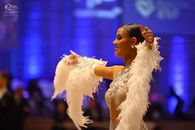 Dancesport competitor: Female dancer: silver sequined latin dress with large white feather accents on t