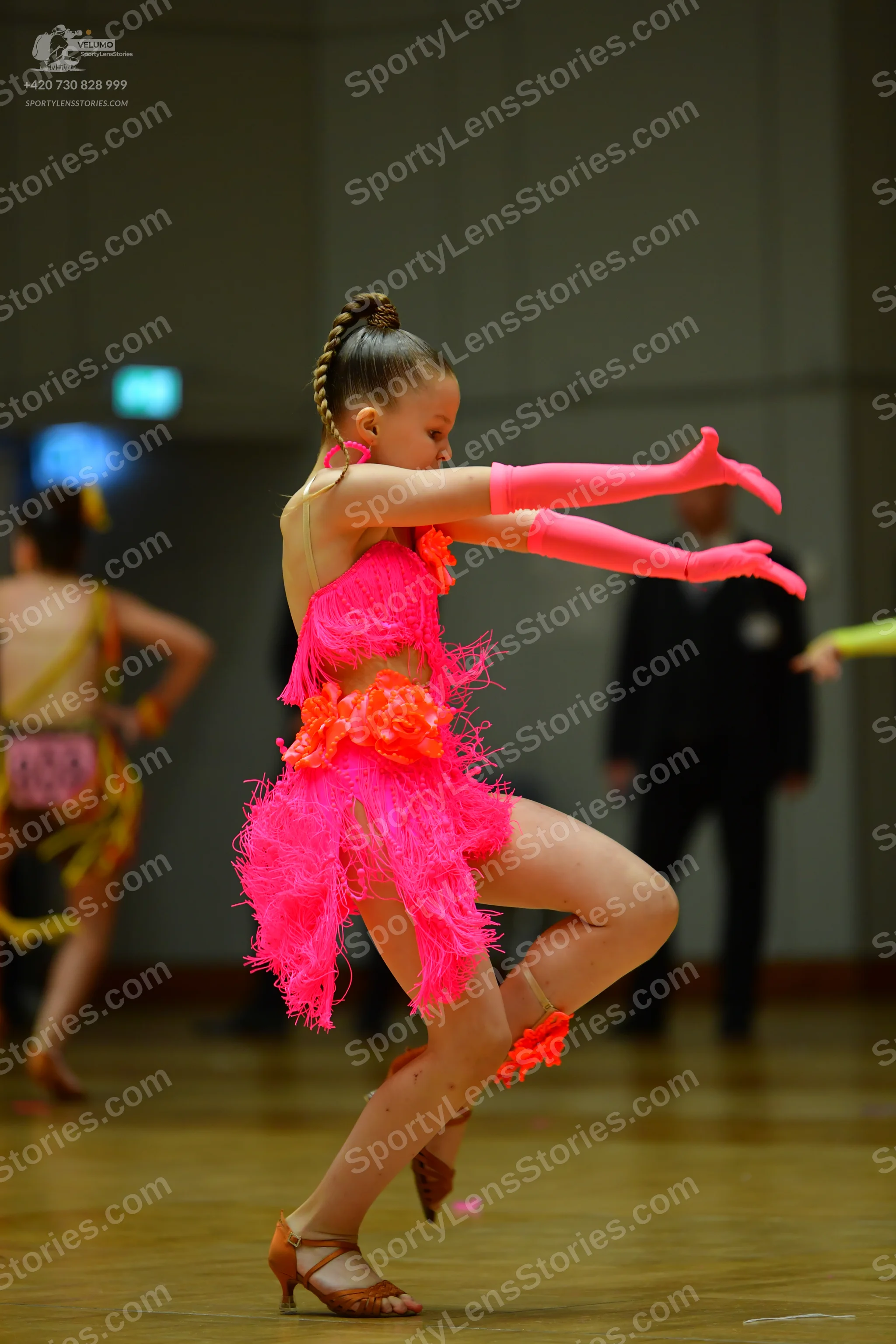 Dancesport competitor: Female dancer in foreground: bright pink latin dress with fringe and orange flor
