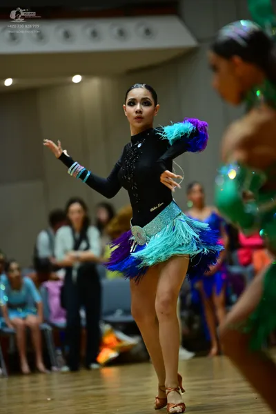 Dancesport competitor: Female dancer: black long-sleeved Latin dress with a teal and purple feathered s