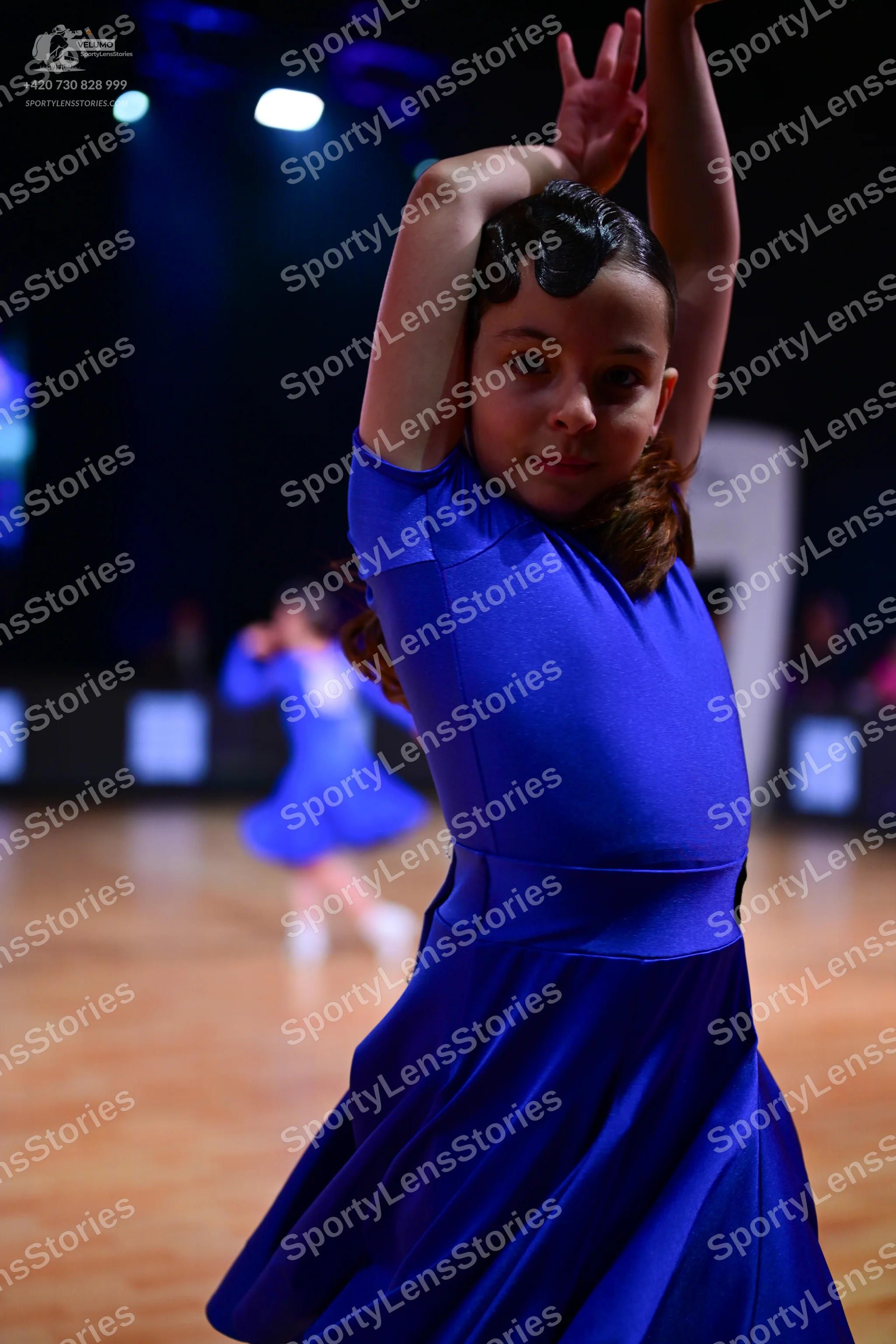 Dancesport competitor: Female dancer in foreground: royal blue satin dress with short sleeves and a ful