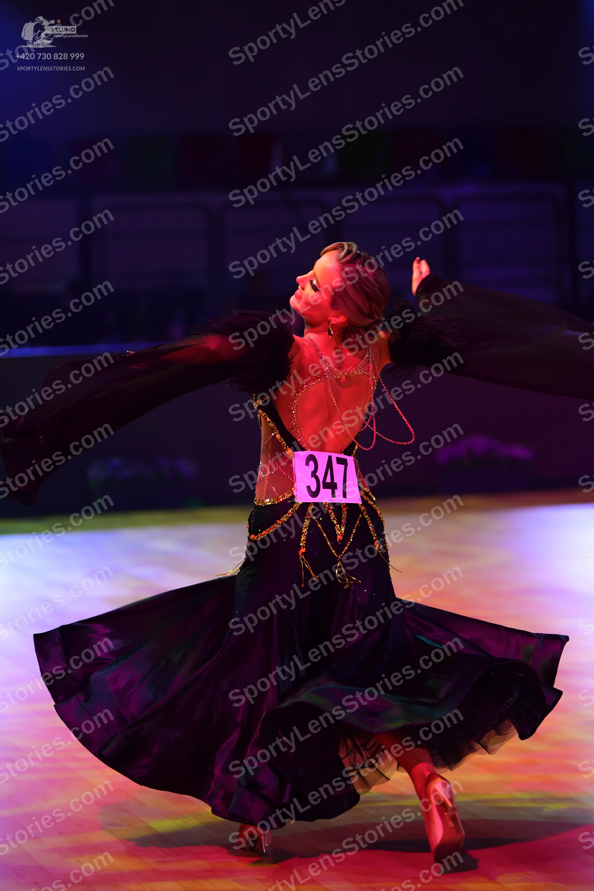 Dancesport competitor: Female dancer: black ballgown with gold chain accents on the back and waist, and