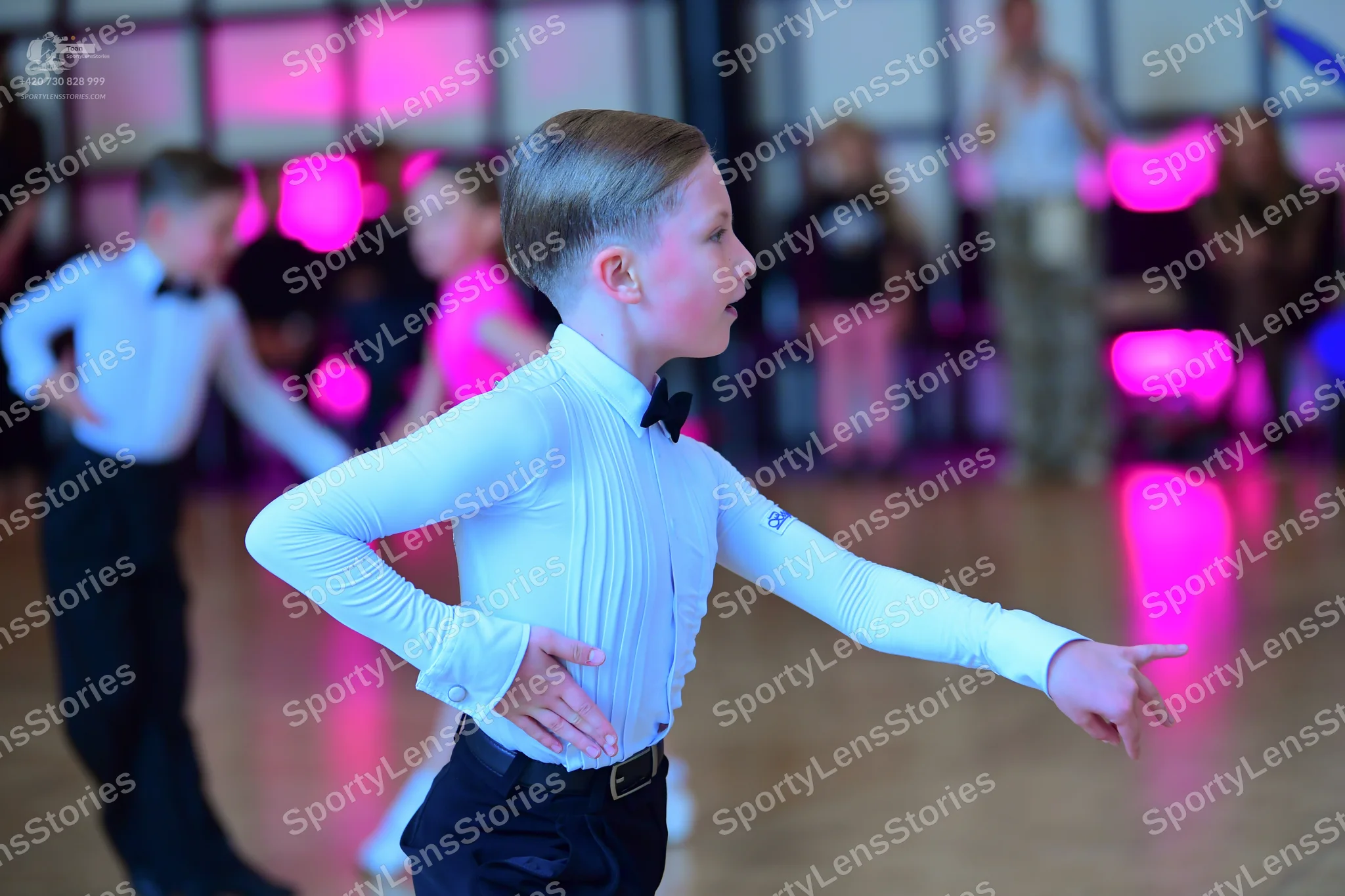 Dancesport competitor: Male dancer in foreground: light blue long-sleeved shirt, black bowtie, and blac