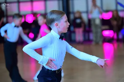 Dancesport competitor: Male dancer in foreground: light blue long-sleeved shirt, black bowtie, and blac