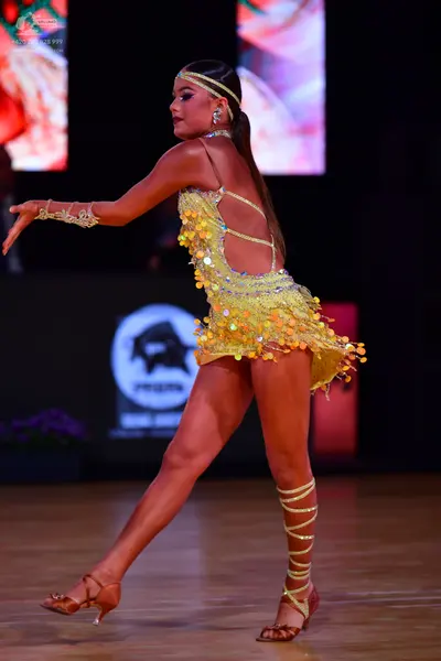 Dancesport competitor: Female dancer: yellow latin dress covered in sequins with a shimmering hem, wear