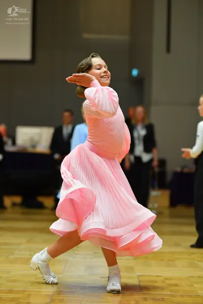 Dancesport competitor: Female dancer: pink, voluminous, multi-layered pleated ballroom dress with long 