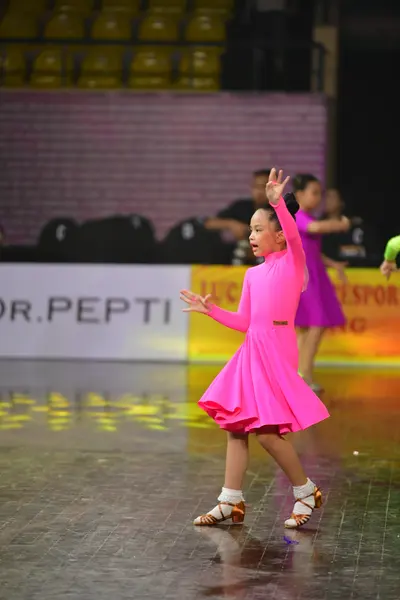 Dancesport competitor: Female dancer 1: bright pink, long-sleeved Latin dance dress with a short, flare