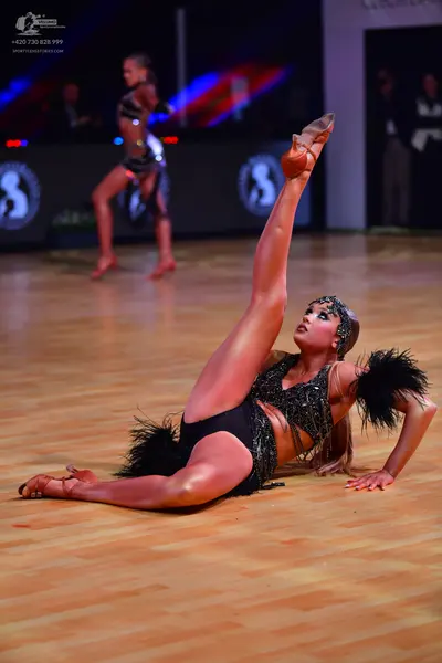 Dancesport competitor: Female dancer in foreground: black sequined latin costume with large black feath