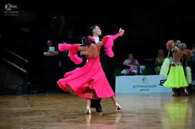Dancesport competitor: Female dancer 1: hot pink Latin dress with large ruffled sleeves and a flared sk