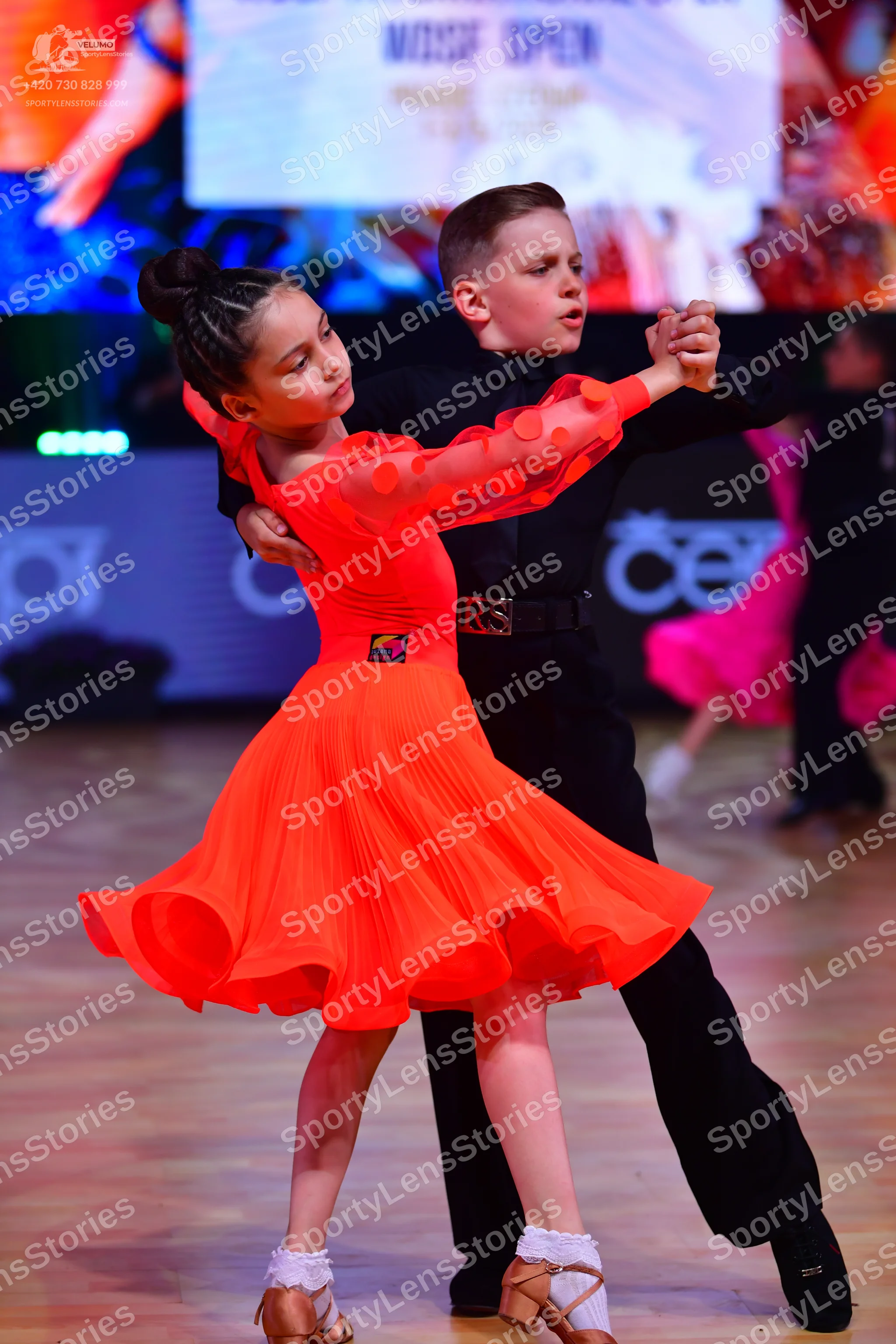 Dancesport competitor: Female dancer: bright orange Latin dance dress with long sleeves featuring small