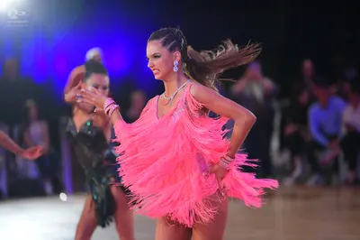 Dancesport competitor: Female dancer: bright pink latin dress with long fringe, silver necklace, and ea