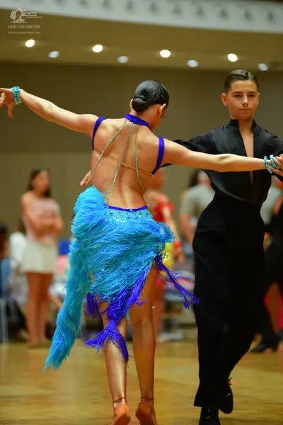 Dancesport competitor: Female dancer: light blue latin dress with long fringe and dark blue straps