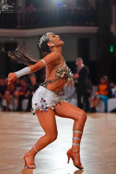 Dancesport competitor: Female dancer: white and tan Latin dance costume embellished with large silver m
