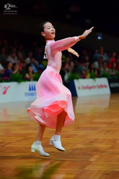 Dancesport competitor: Female dancer: pink long-sleeved ballroom dress with a flowing skirt and white d
