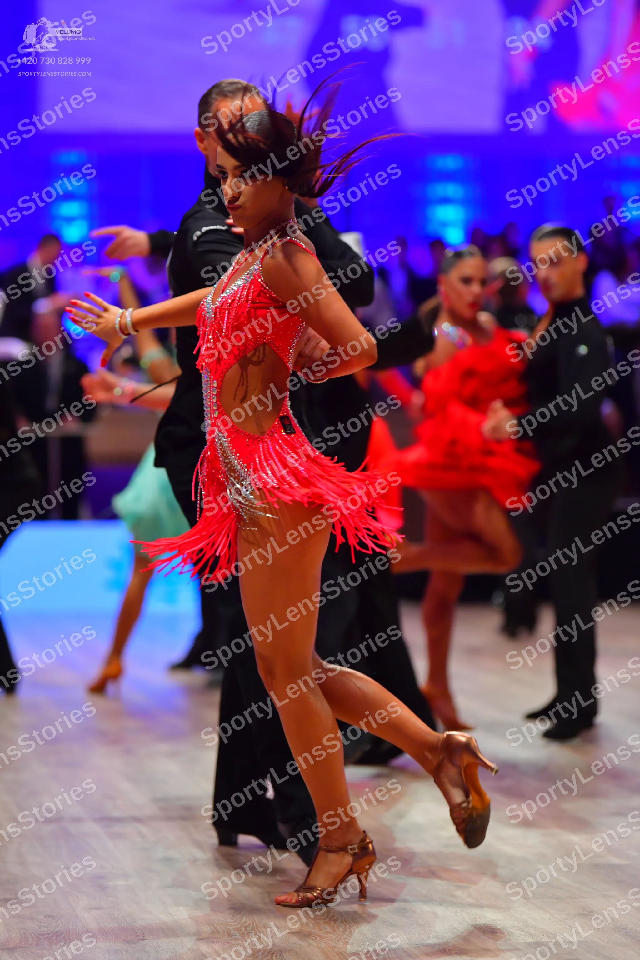 Dancesport competitor: Foreground female dancer: fuchsia Latin dress with fringe