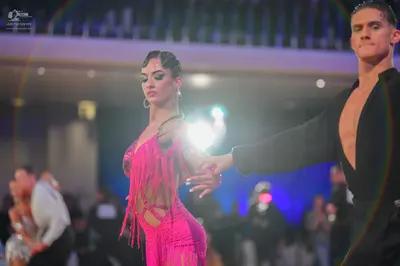 Dancesport competitor: Female dancer: bright pink Latin dance dress featuring fringe and cutouts, paire