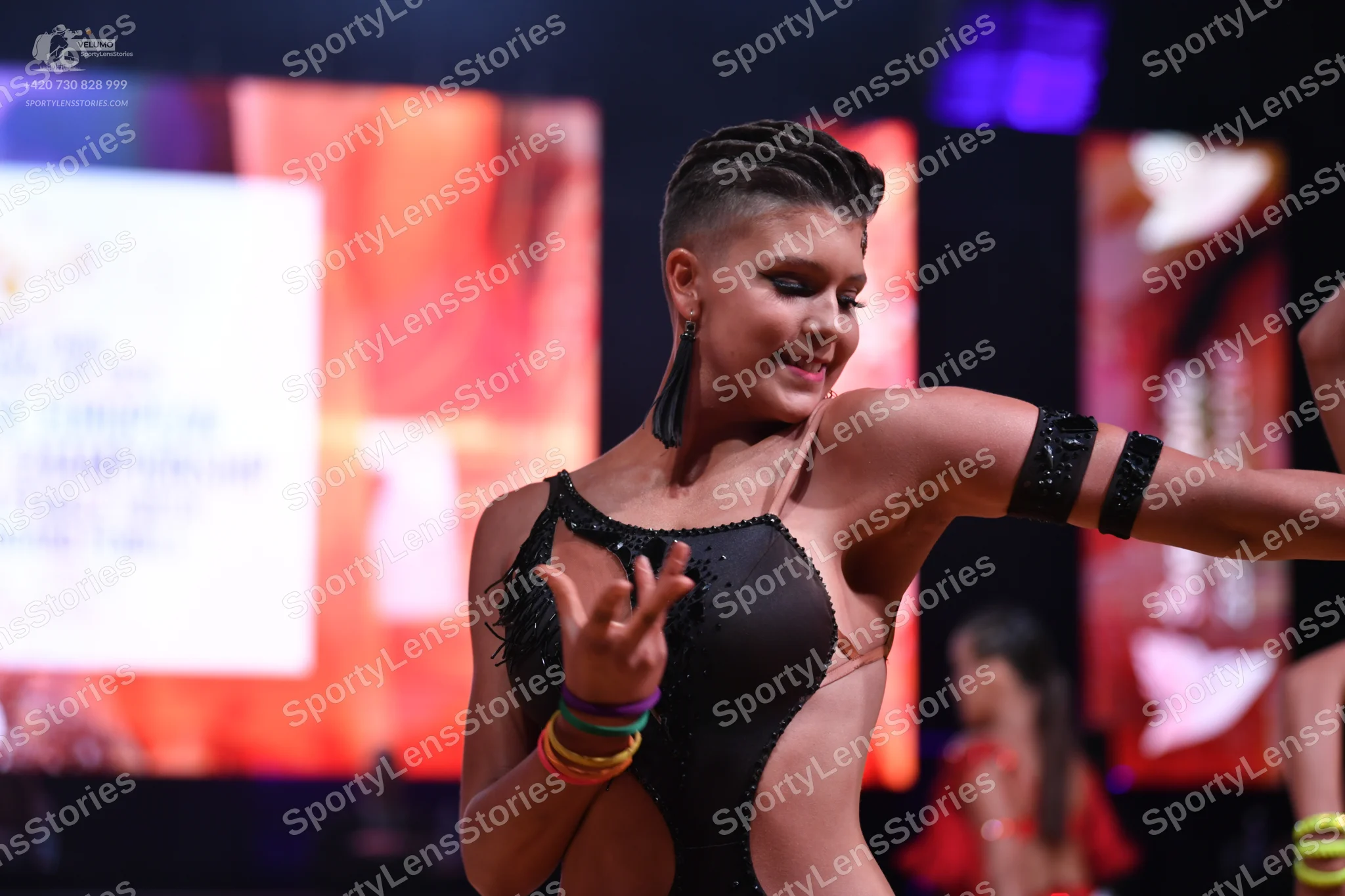 Dancesport competitor: Female dancer in foreground: black latin dance bodysuit with rhinestones and bla